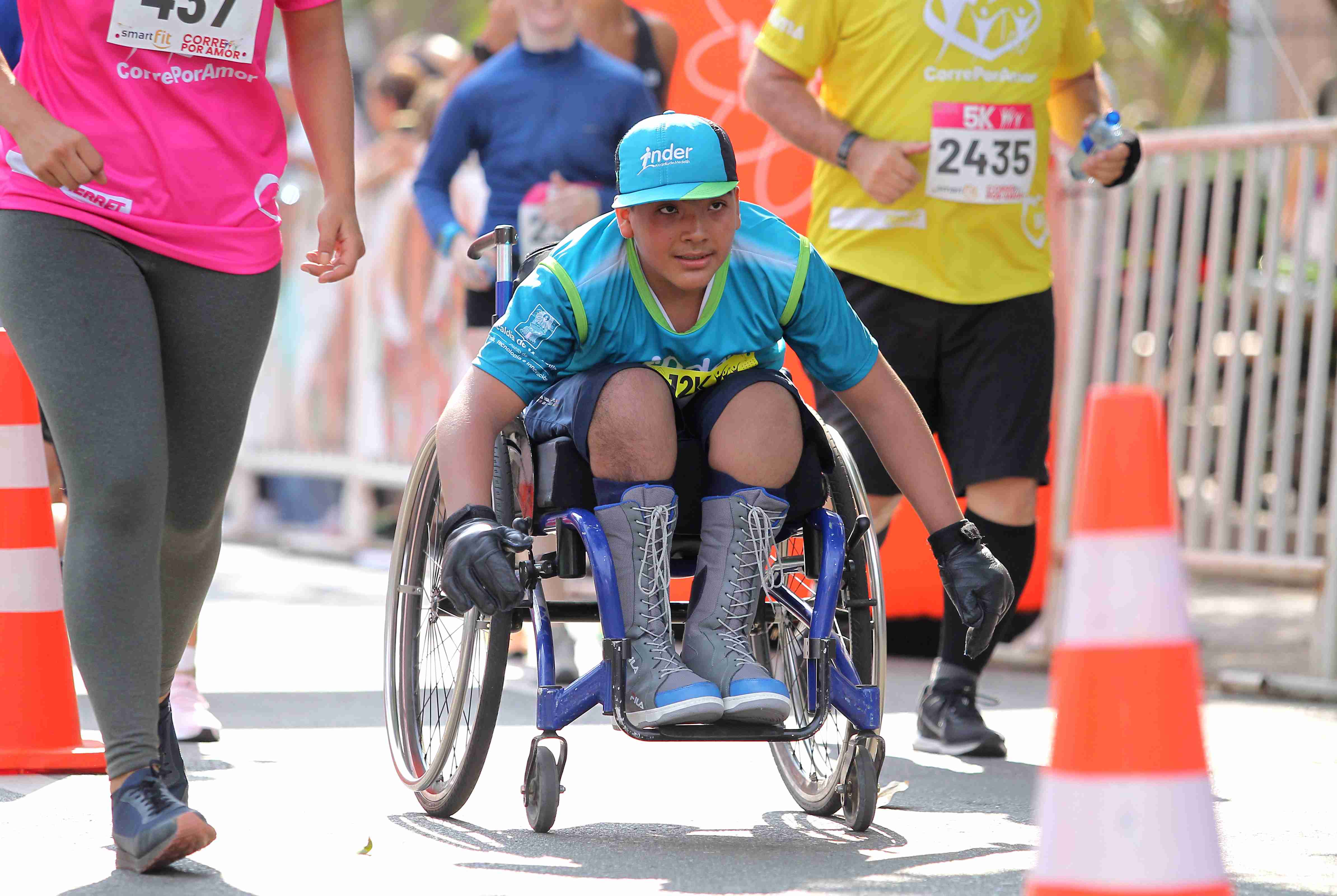 Joven con la camiseta del Inder Medellín participando de la carrea en silla de ruedas de la carrera.